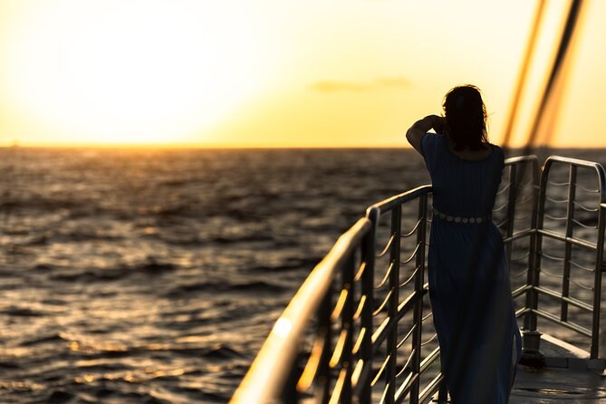 A passenger at the bow of a boat as the sun sets over the sea