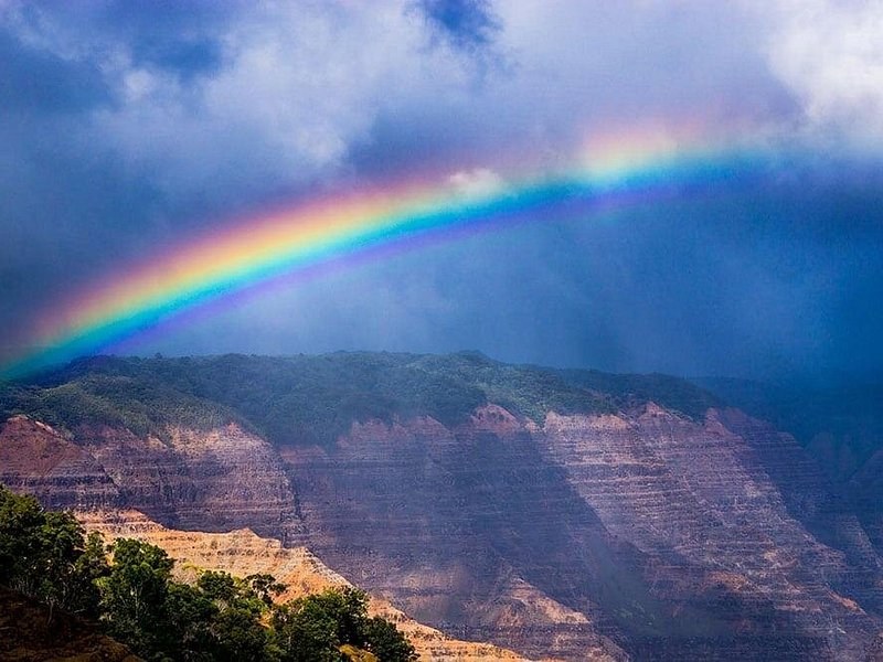 A rainbow over the red and green walls of a deep canyon