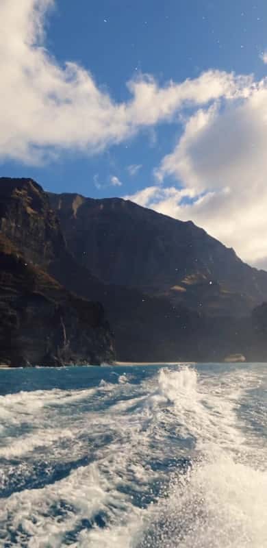 A boat's white wake below dark cliffs and a blue sky